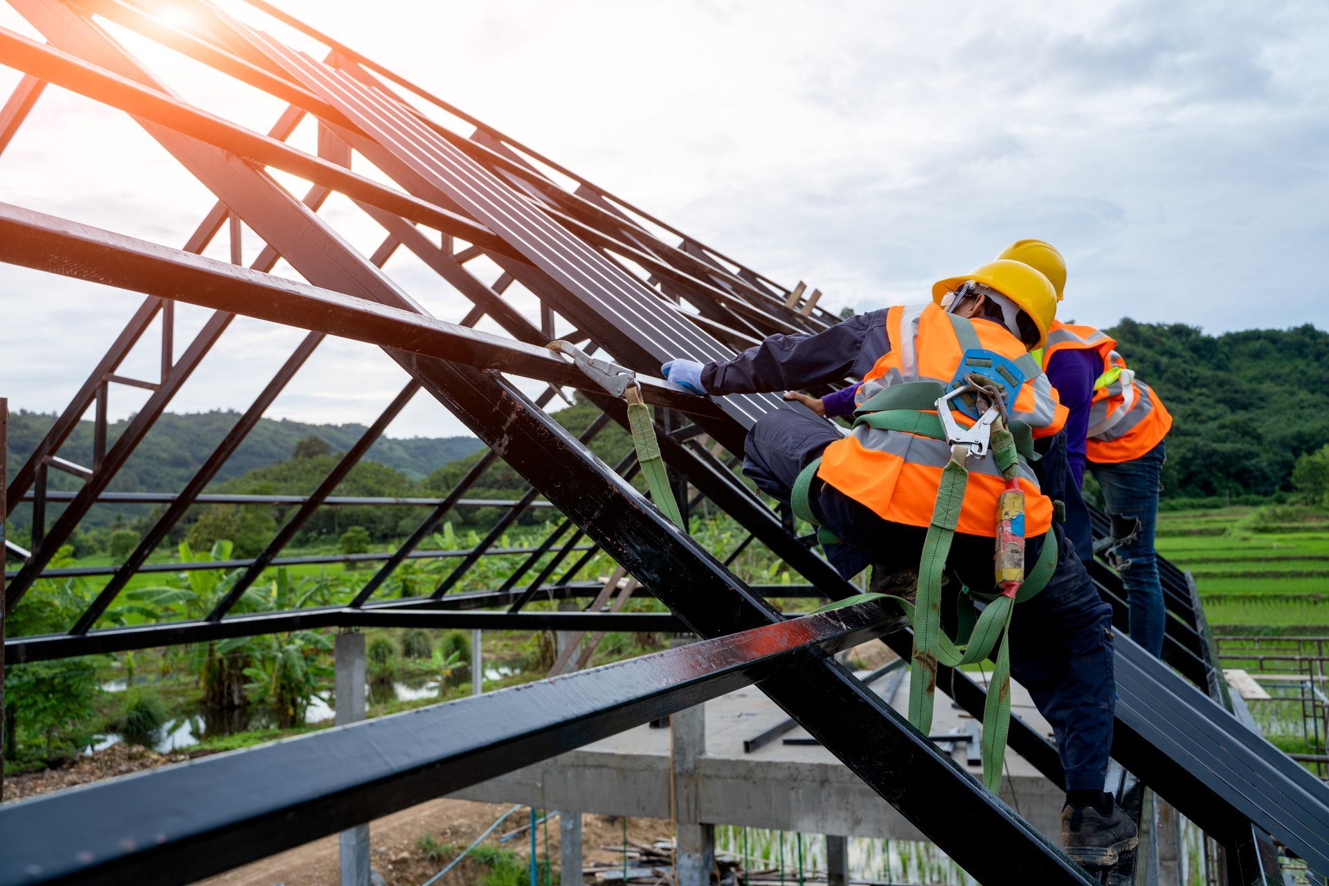 Construction workers in safety harnesses install panels on a metal roof frame.