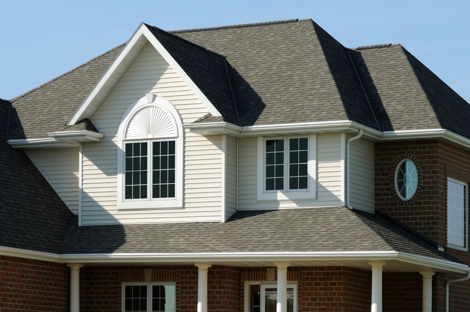 Two-story brick house with a dark gray shingled roof, white siding, and several windows.