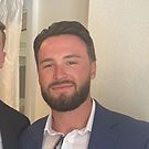 Man in blue blazer with dark beard, smiling, looking at the camera.