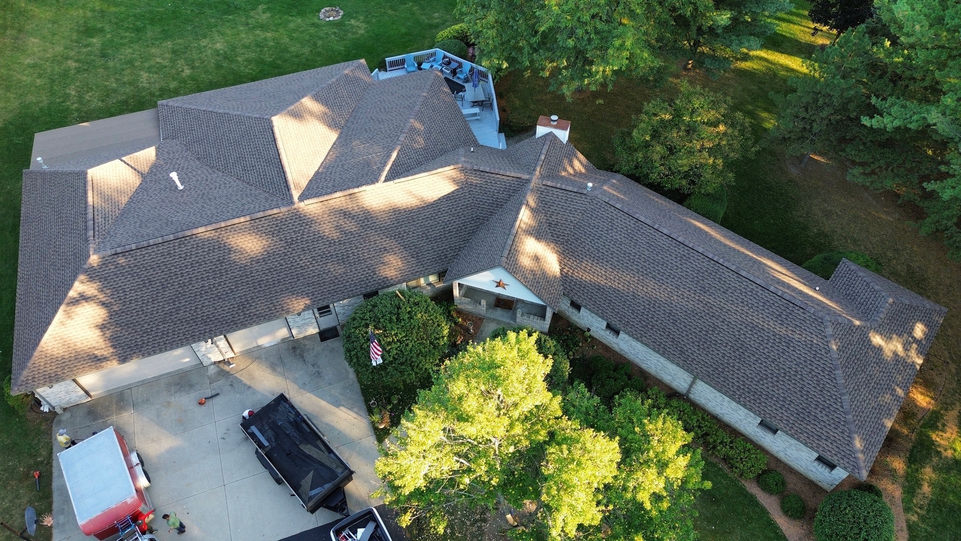 Overhead view of a house with a brown shingle roof, surrounded by green trees and a driveway.