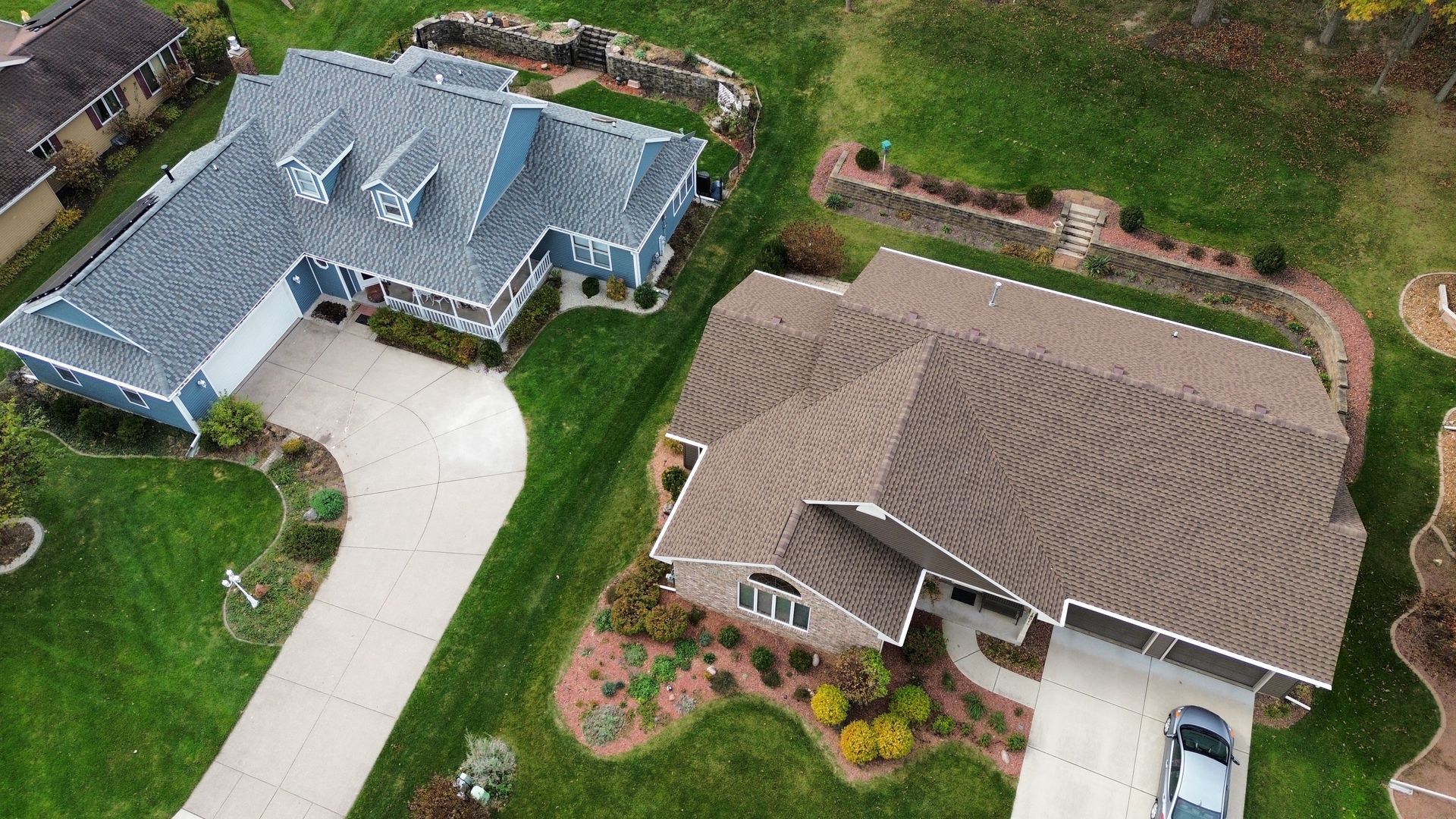 Two houses with driveways, surrounded by green lawns. One house blue, the other brown.