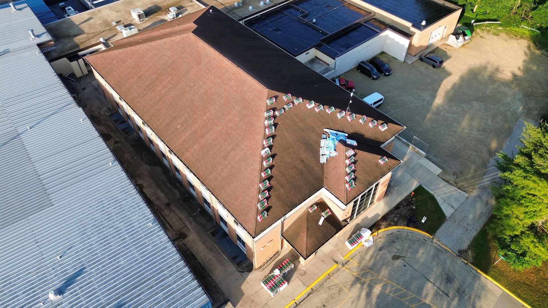 Aerial view of a brown-roofed building with several cars parked nearby on a sunny day.