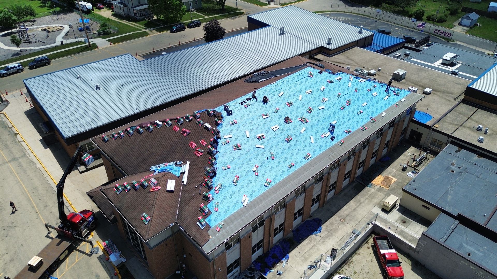 Aerial view of a building roof under construction with blue tarps and workers.