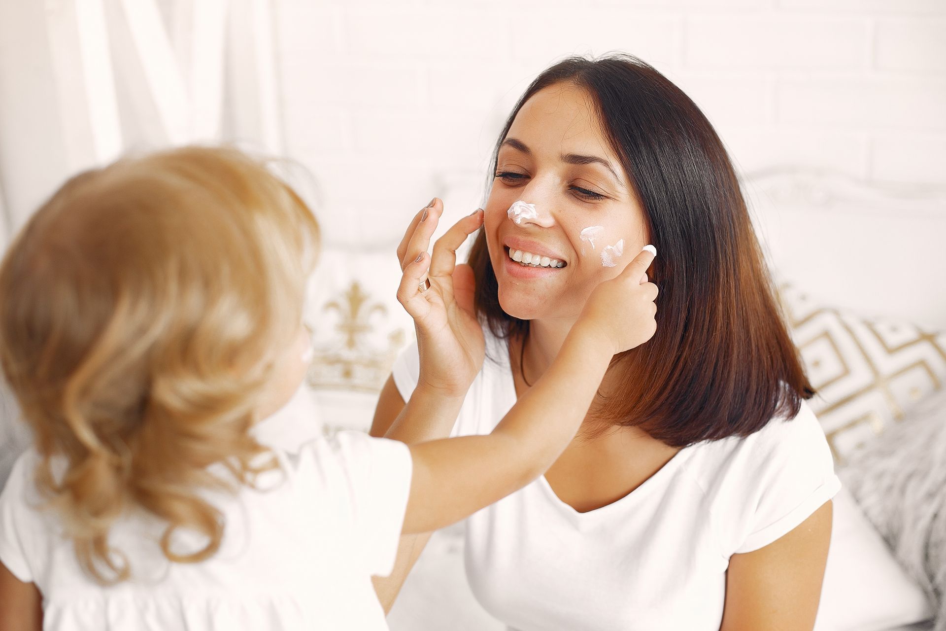 A little girl is putting cream on a woman 's face.