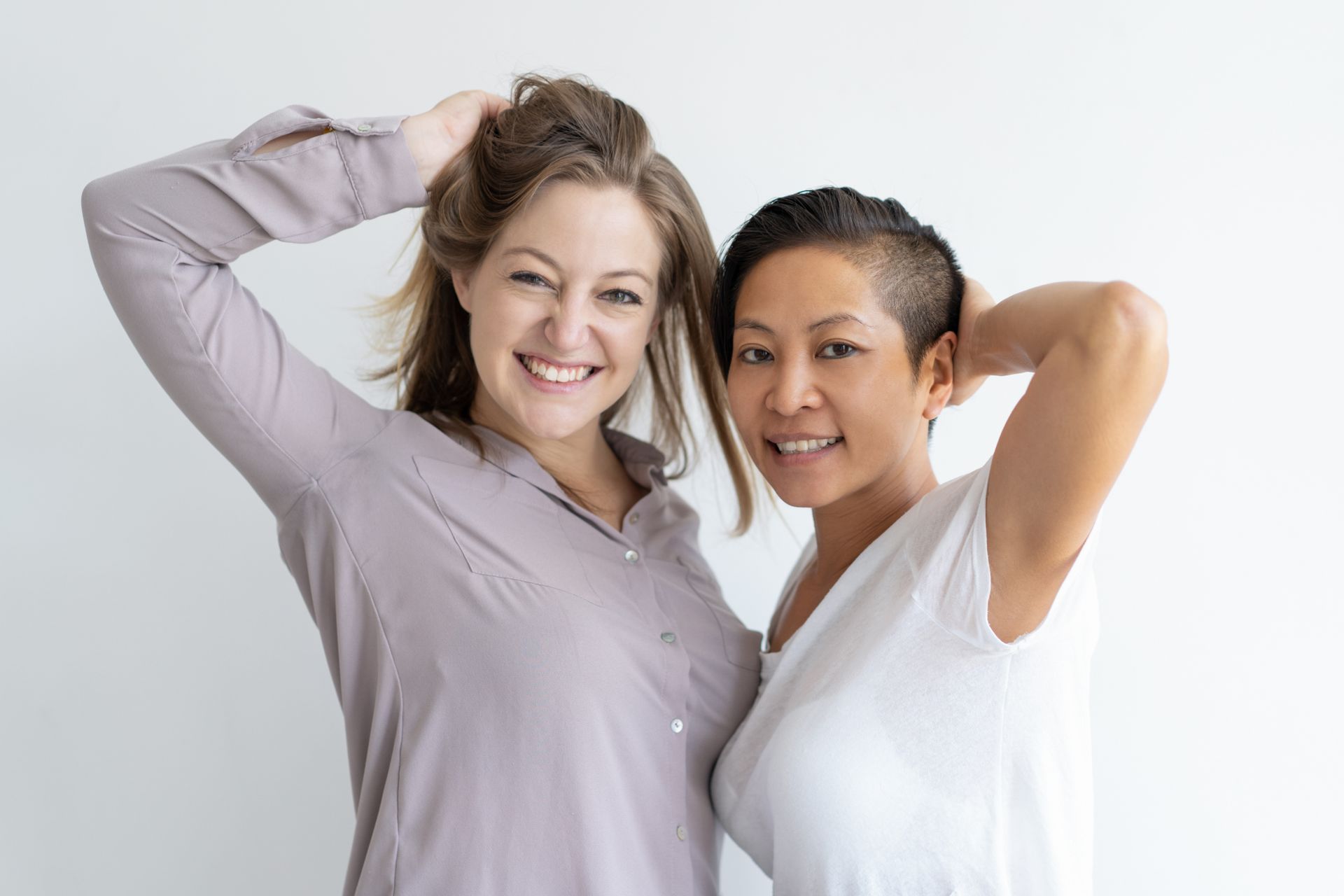 Two women are standing next to each other with their hands in their hair.