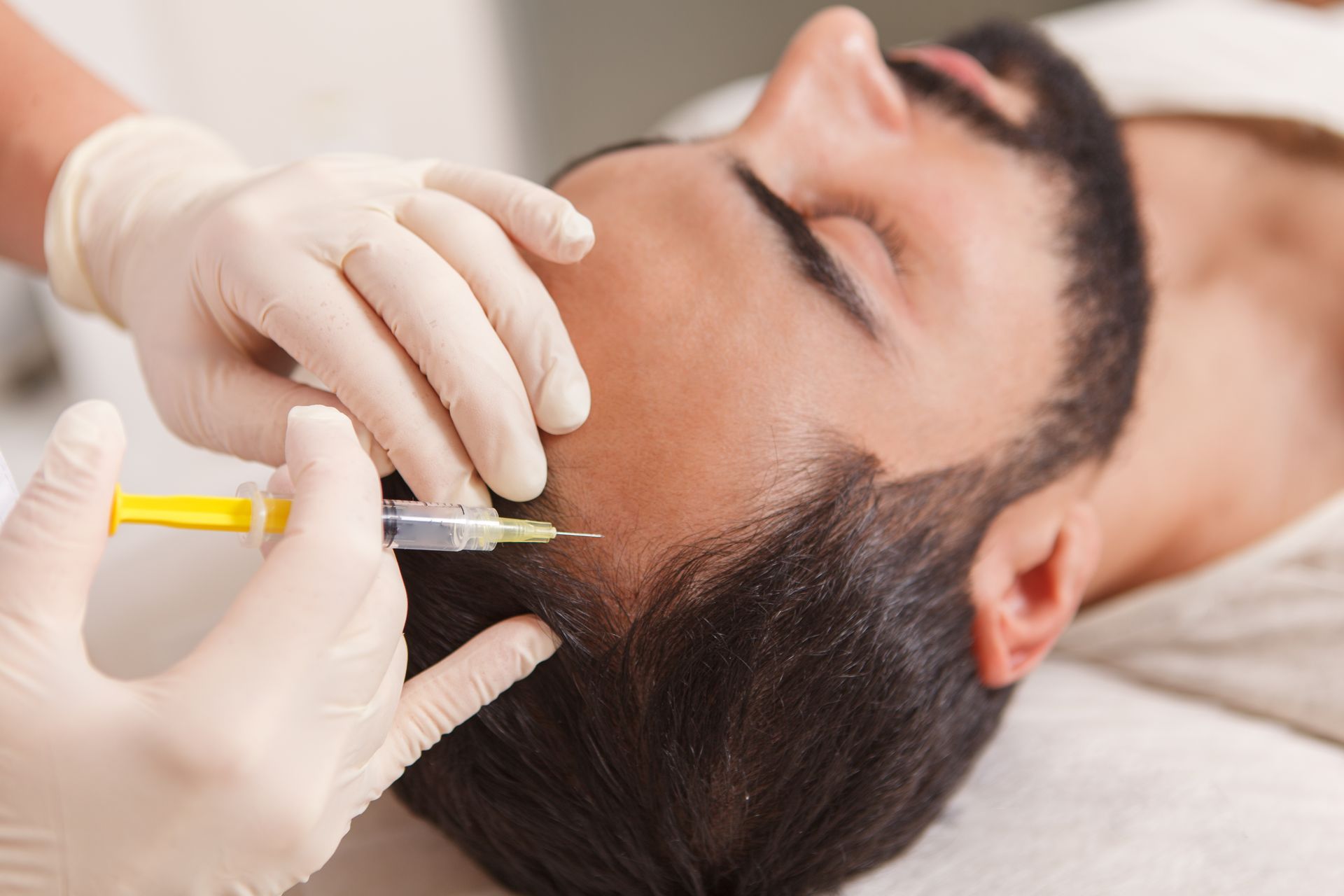 Gloved practitioner injecting a man’s cheek with a syringe during a cosmetic procedure