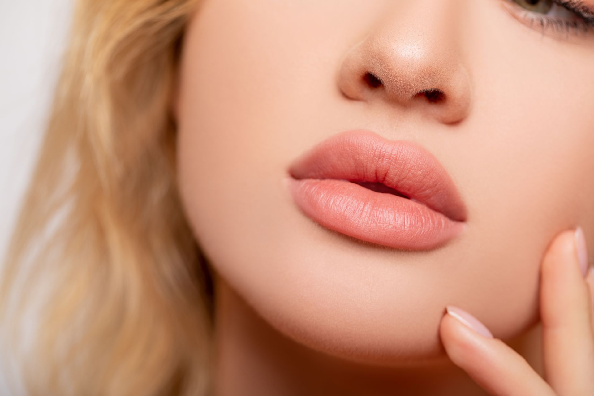 Close-up of a person's face; full, pink lips, soft skin, and light blonde hair.