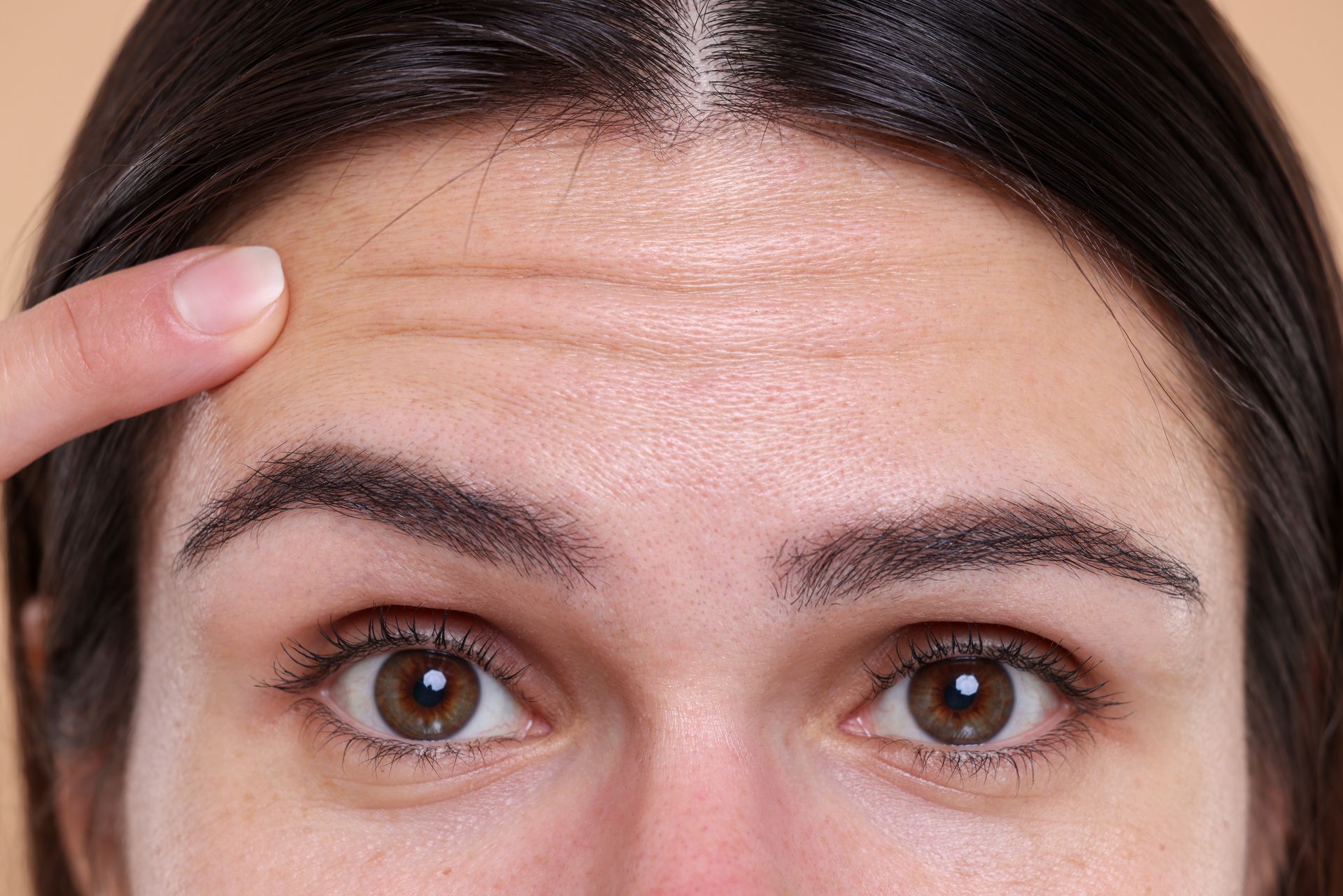 Close-up of a person’s forehead and eyes, with a finger pointing at horizontal forehead wrinkles.