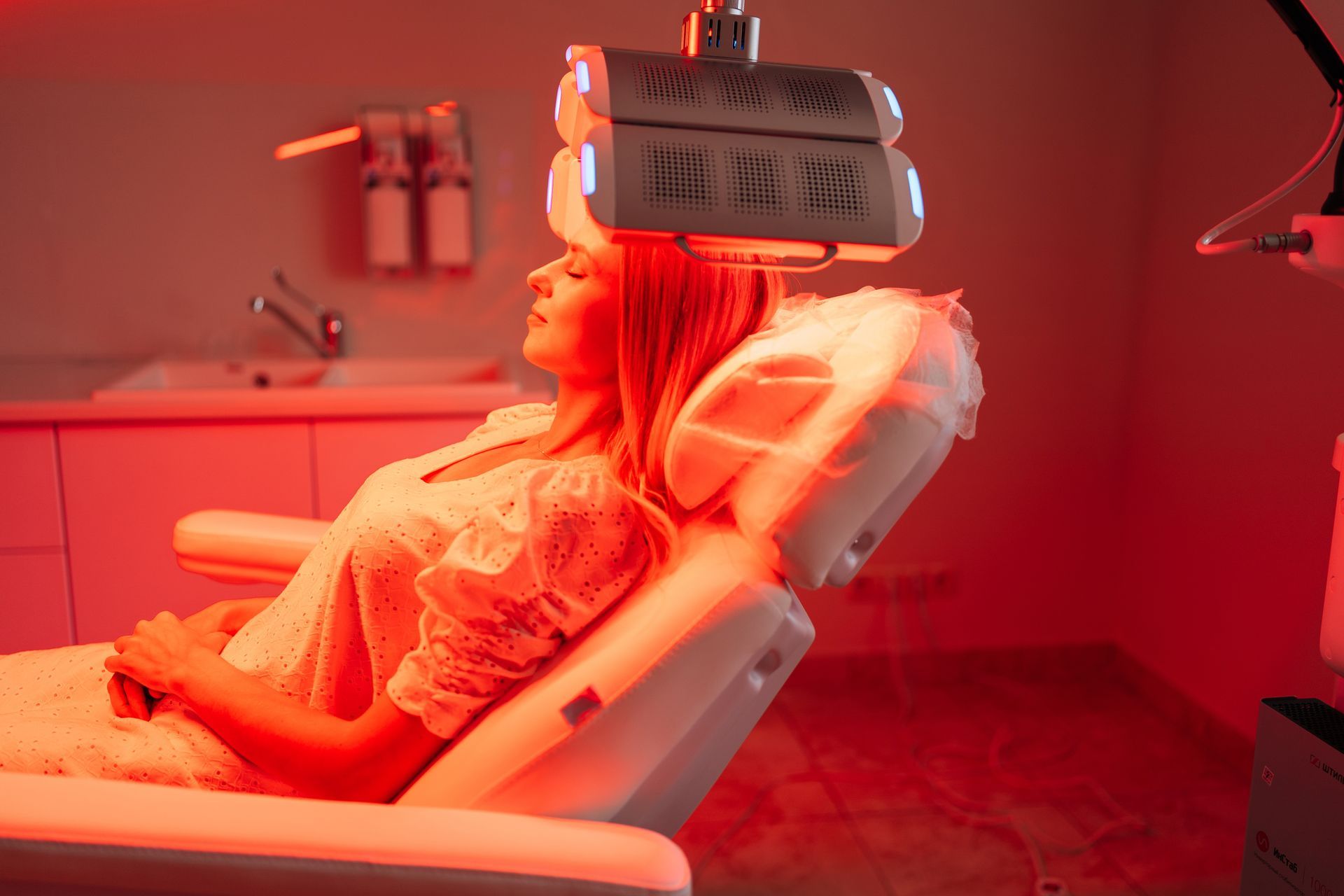 A woman is sitting in a chair with red lights on her head.