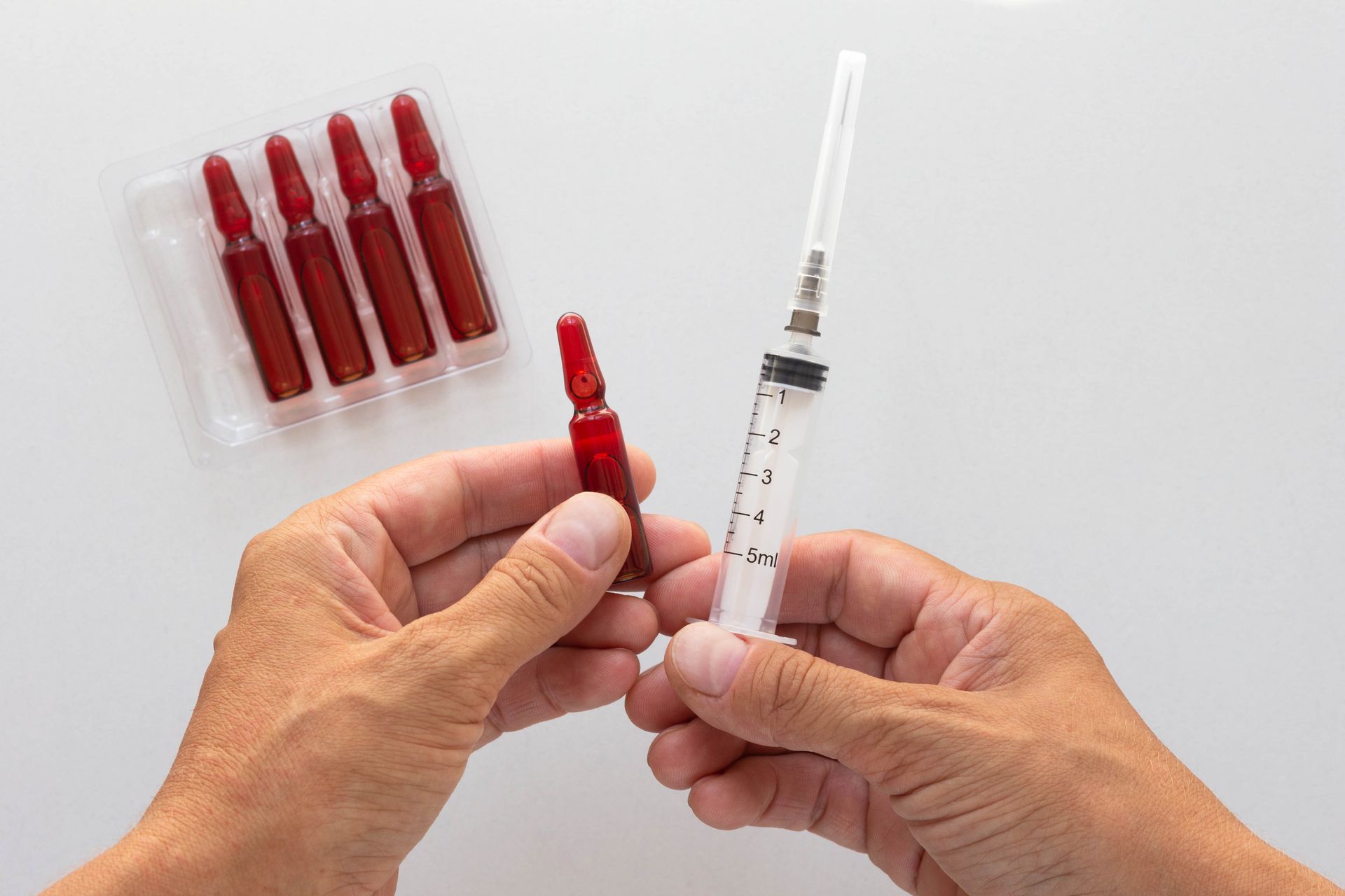 A person is holding a syringe and an ampoule in their hands.