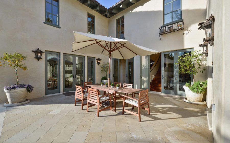 Sunny courtyard patio with wooden dining table, chairs, and umbrella in front of a stucco house