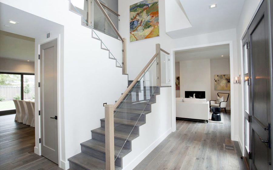 Modern home entryway with gray stairs, white walls, wood floors, and a living room visible beyond.