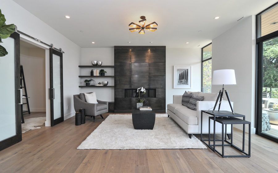Modern living room with gray sofa, black accent wall, desk, rug, and large windows