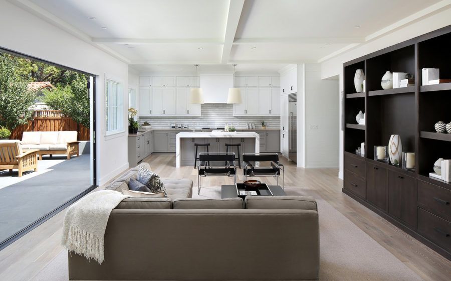 Bright open living room and kitchen with gray sofa, white walls, black shelving, and sliding doors to patio