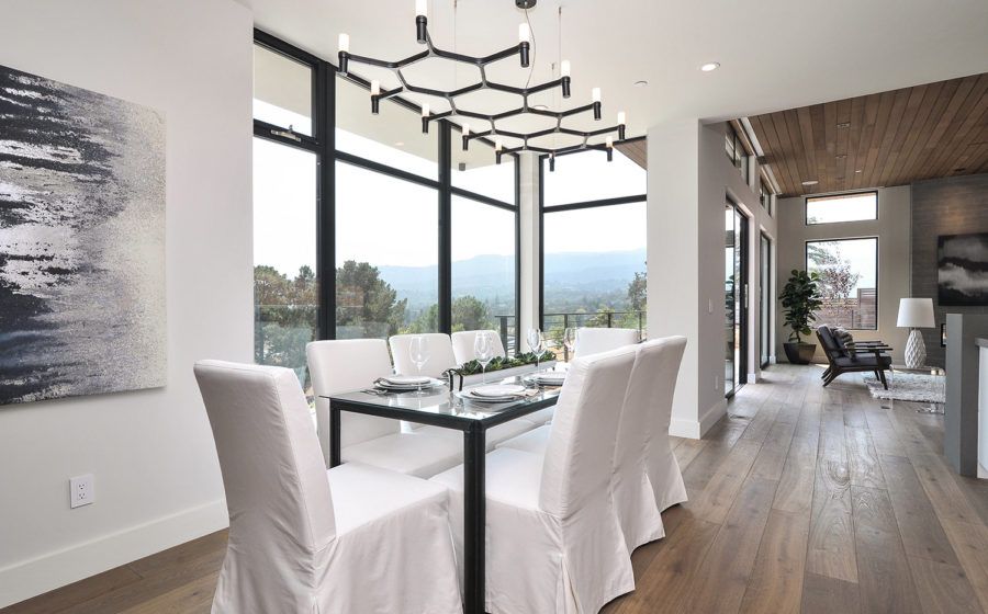 Modern dining room with white chairs, glass table, large windows, and mountain view