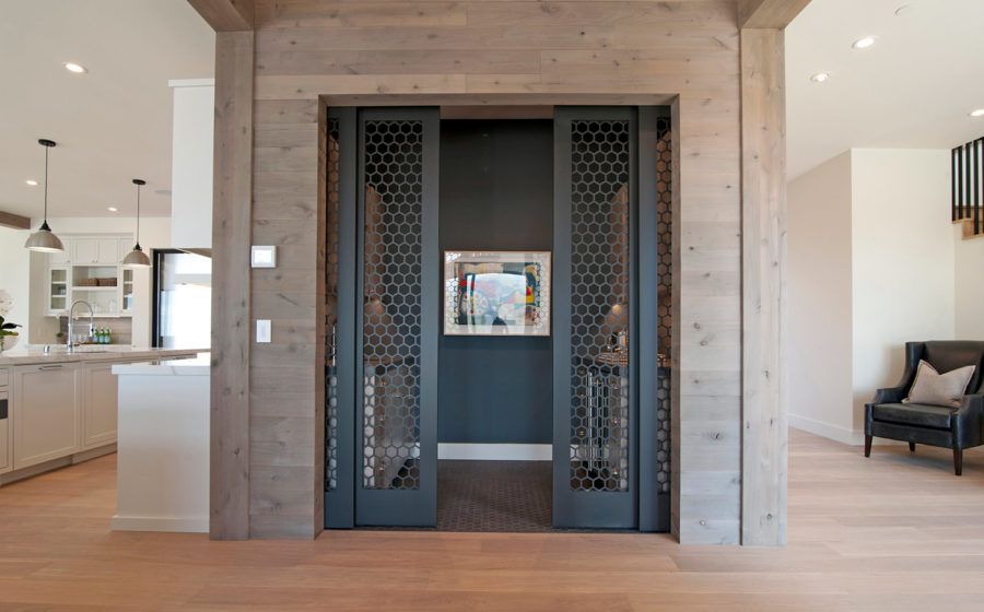 Modern home elevator with dark mesh doors in a wood-paneled interior hallway