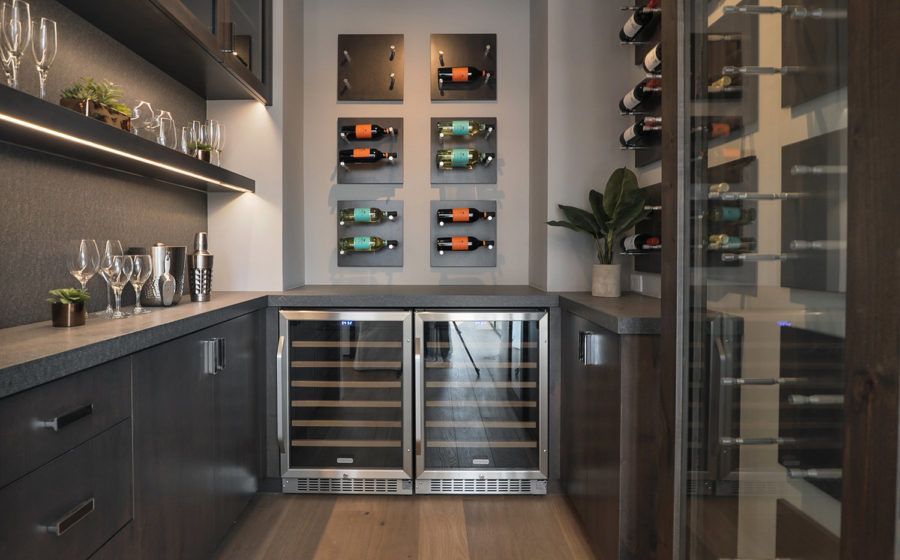Modern wine cellar with wall-mounted racks, glass door, and dark cabinetry, featuring rows of wine bottles.