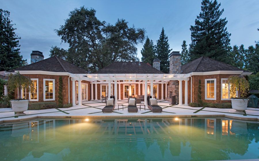 Luxury house with lit patio and pool at dusk, reflected in calm water