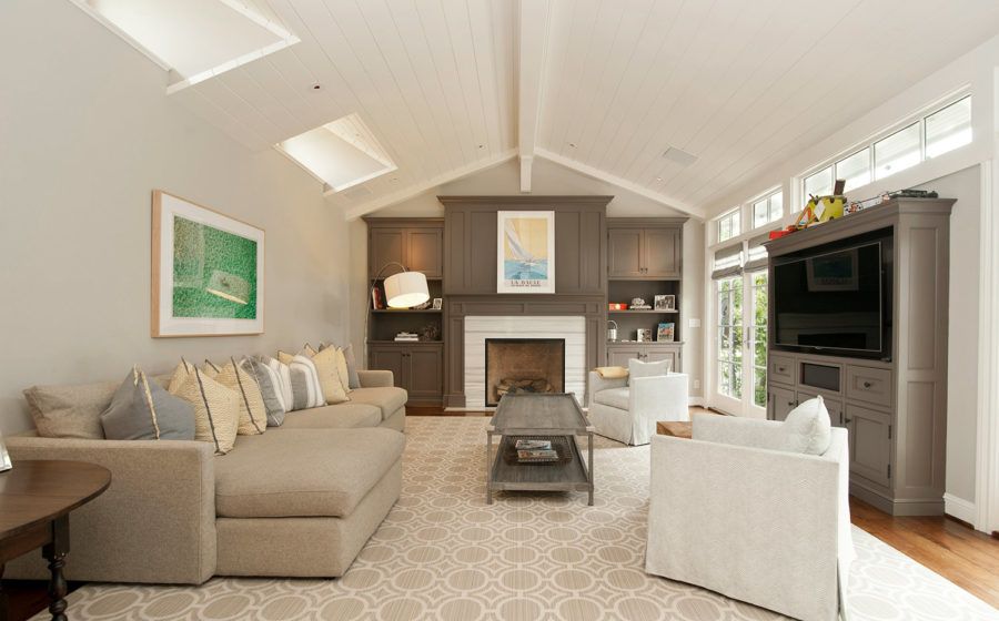 Bright living room with beige sofa, fireplace, white chair, and dark TV cabinet under vaulted ceiling
