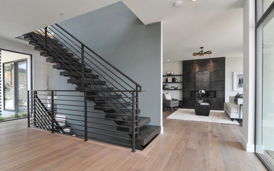 Modern open interior with black staircase, light wood floors, and a living area in the background