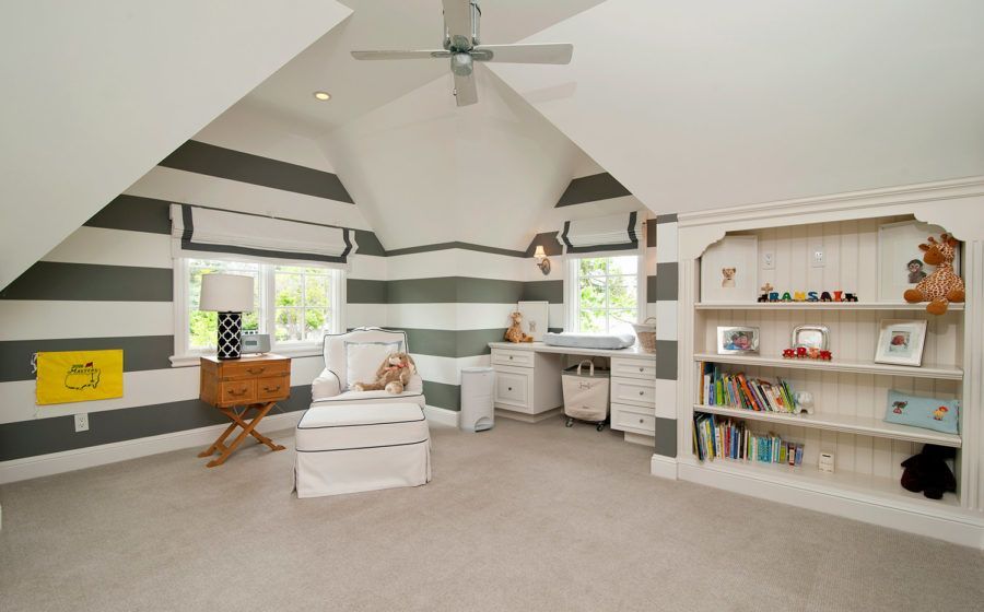 Spacious nursery with gray-and-white striped walls, white furniture, a ceiling fan, and a bookshelf.