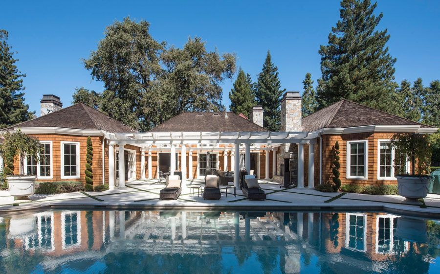 Luxury house with a large swimming pool and lounge chairs in a sunny wooded backyard