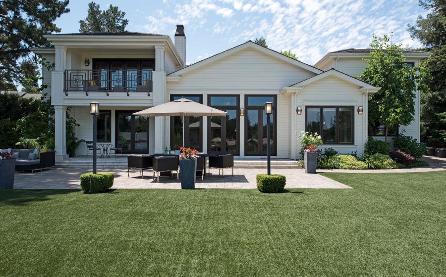 Modern house with large patio, umbrella table, and manicured green lawn under a bright sky