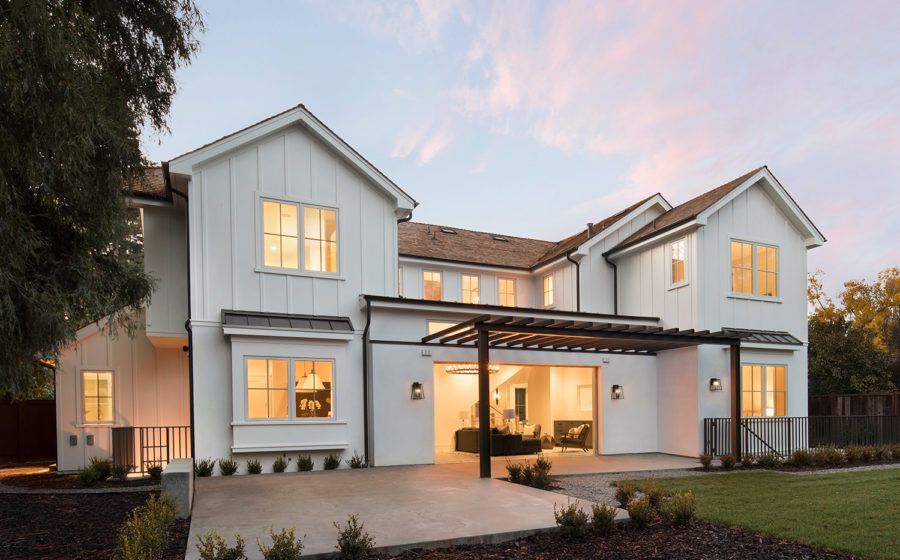 Modern white two-story house with lit windows and a covered patio at dusk