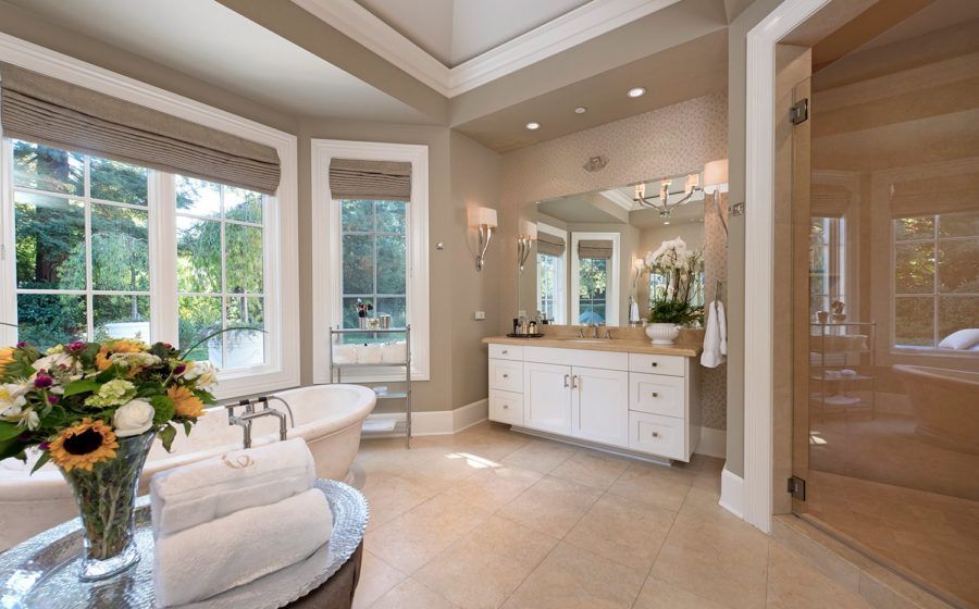 Bright bathroom with large windows, white vanity, soaking tub, and beige tile floor