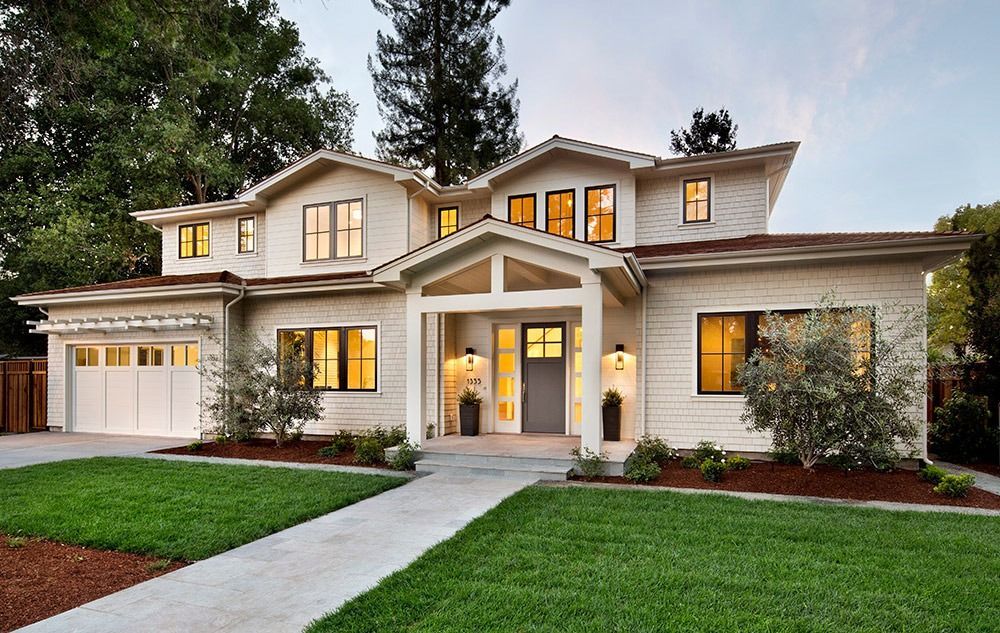 Two-story suburban house with a front porch, lit windows, garage, and green lawn at dusk
