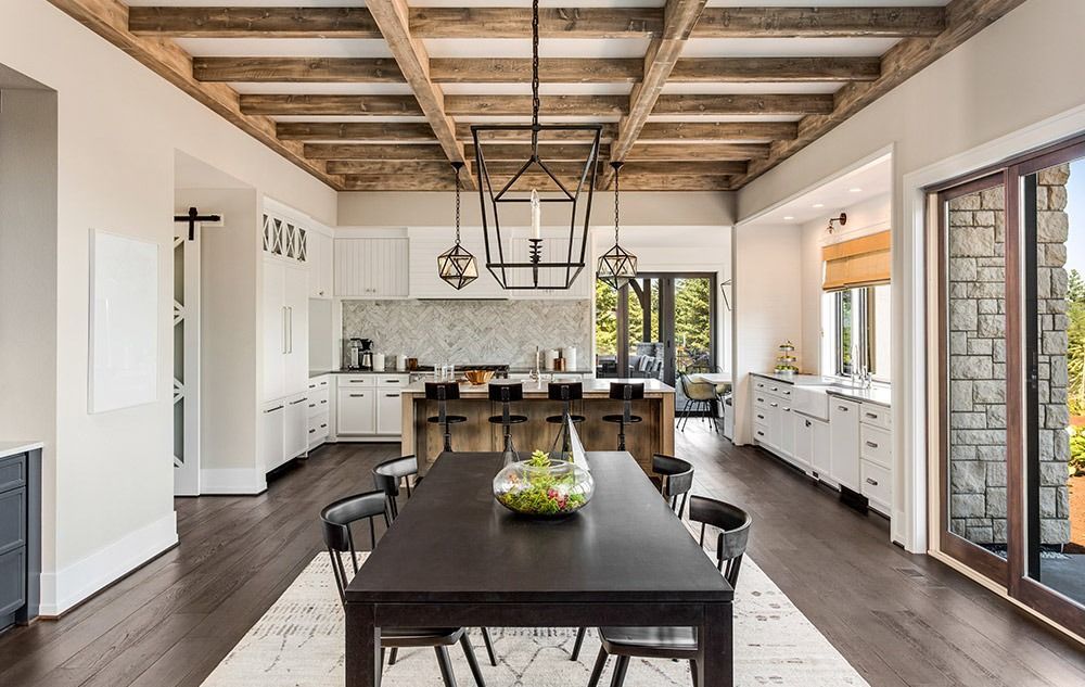 Bright modern kitchen with dark dining table, white cabinets, and exposed wood-beam ceiling