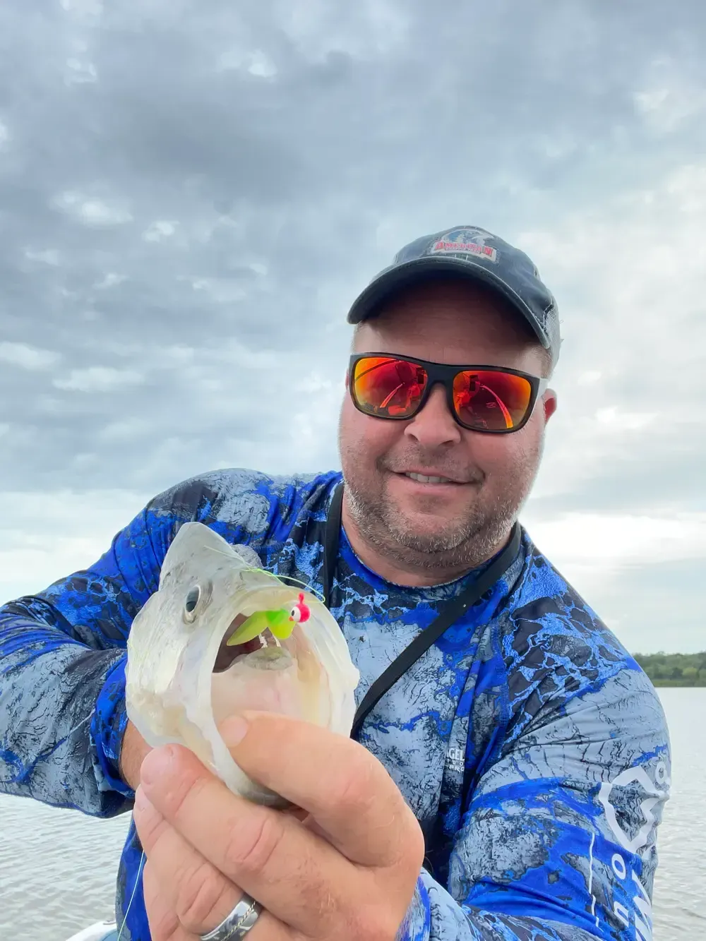A man wearing sunglasses and a hat is holding a fish in his hands.
