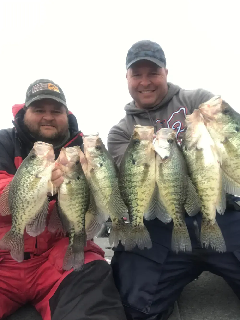 Two men are holding a bunch of fish in their hands.