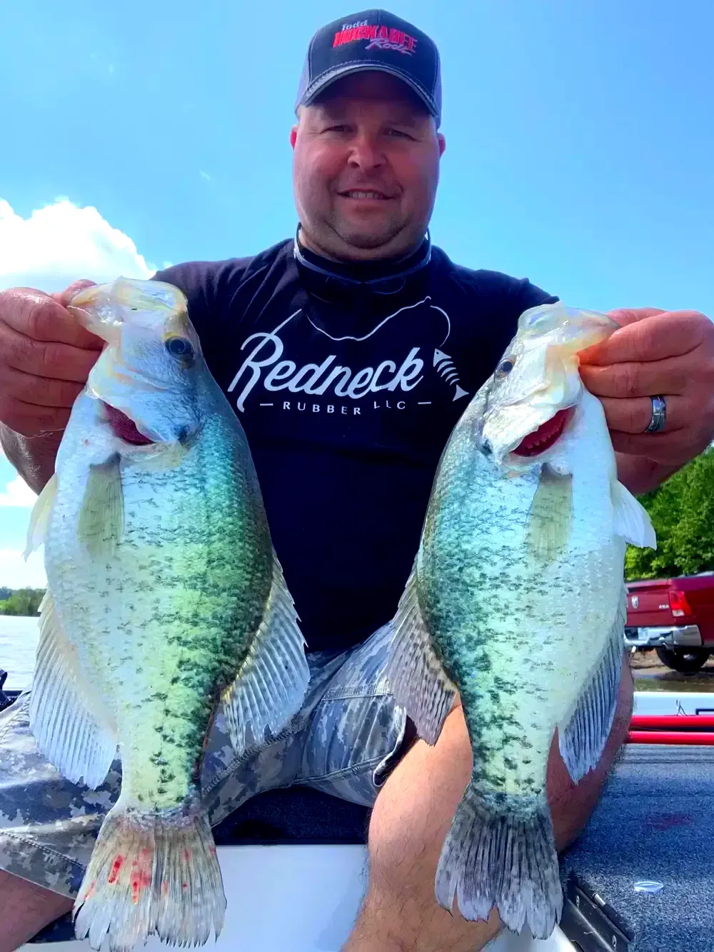 A man wearing a redneck shirt is holding two fish