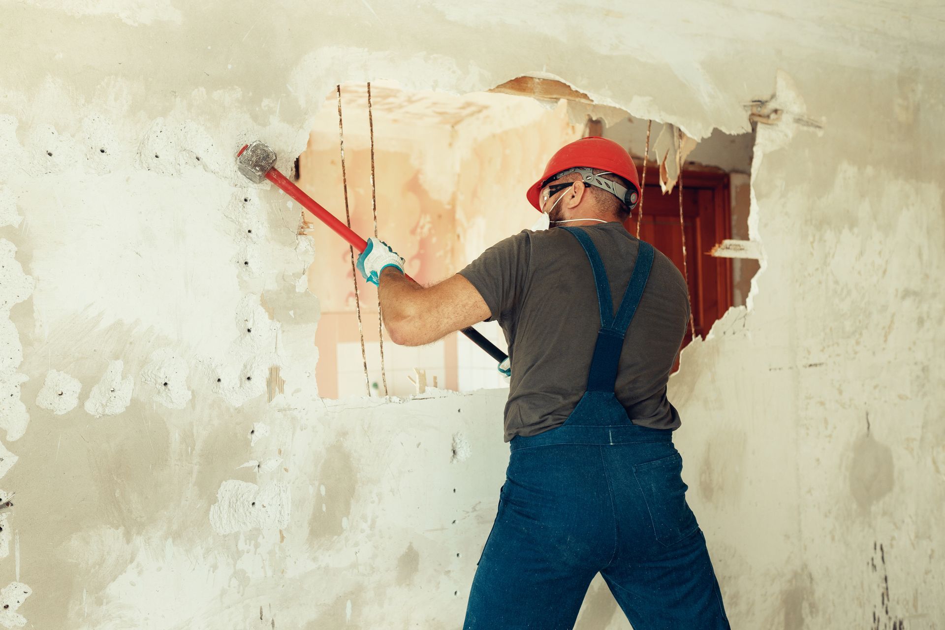Construction worker using sledgehammer to demolish interior wall during renovation.