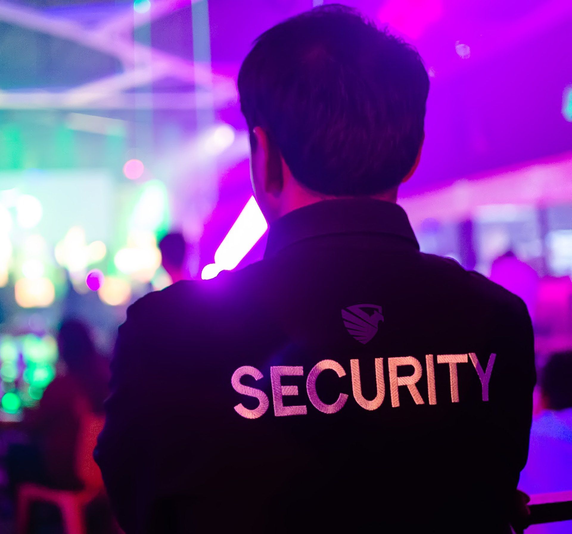 A man wearing a security jacket is standing in front of a crowd.