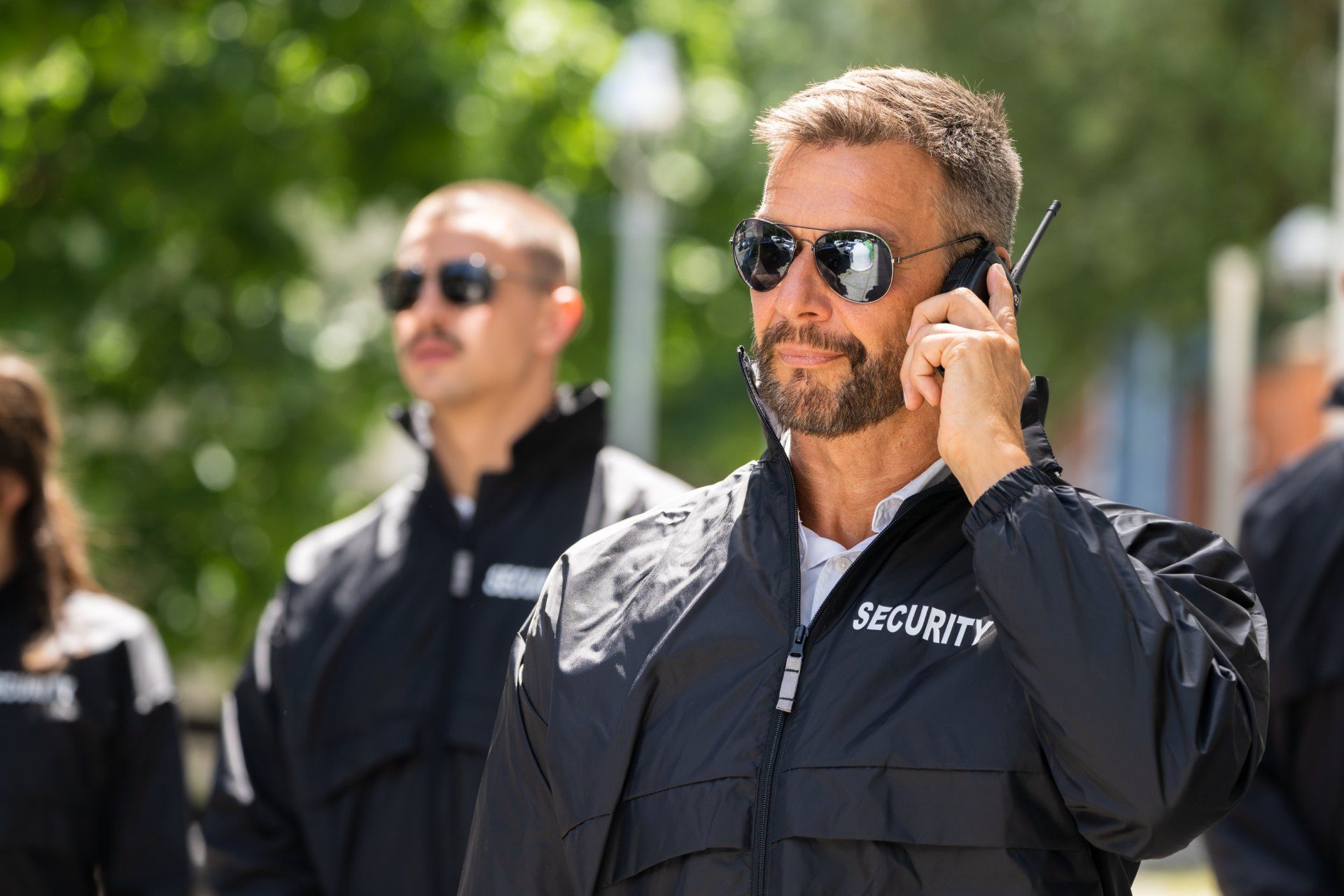 A security guard is talking on a cell phone while wearing sunglasses.