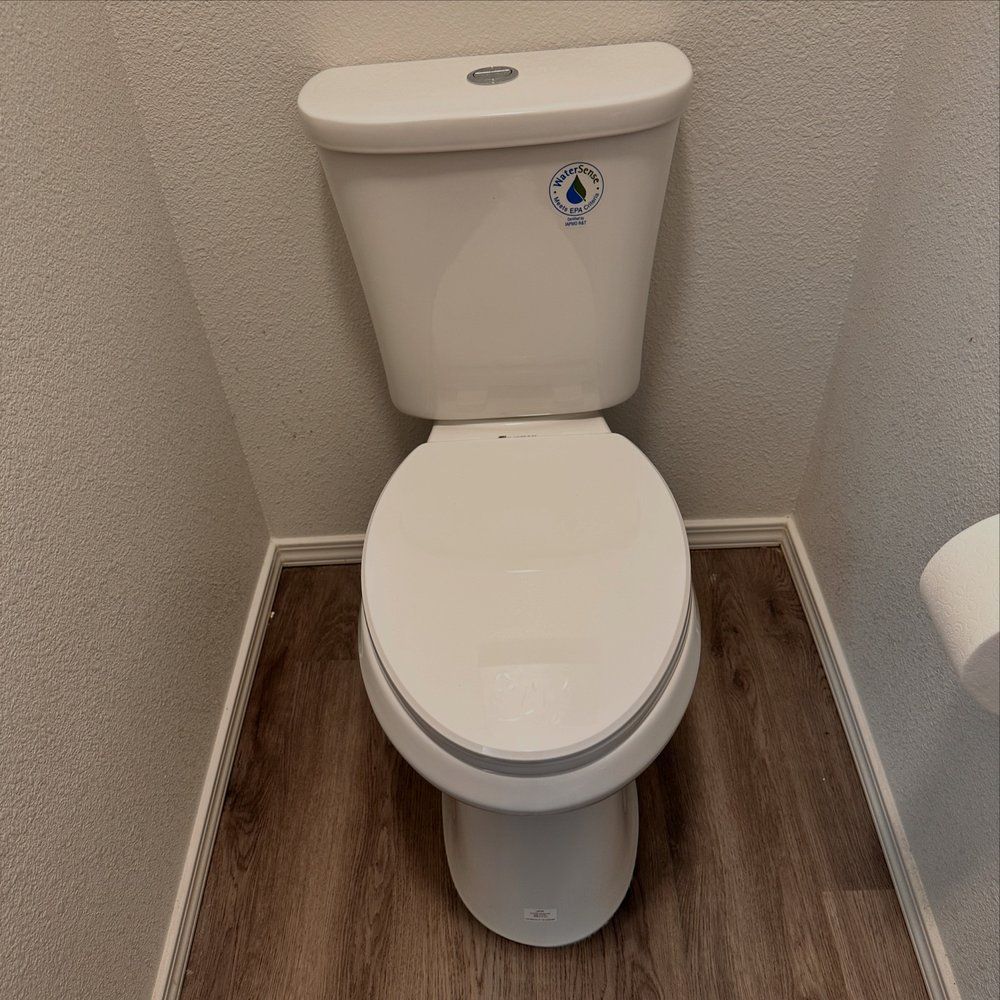 White toilet in a small bathroom with wood-look flooring and light-colored walls.