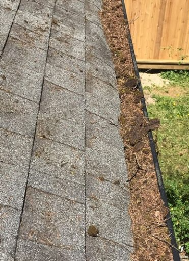 A close up of a gutter on a roof with a wooden fence in the background.