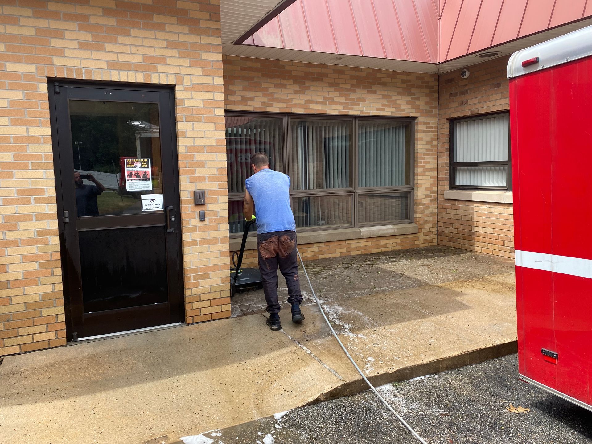A man is cleaning the sidewalk outside of a building.