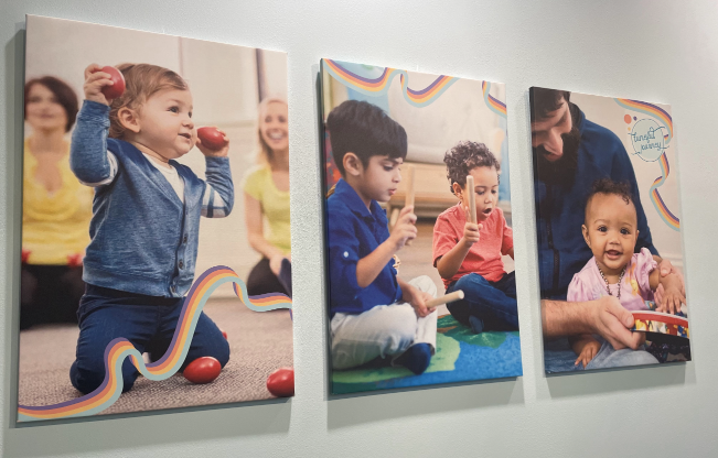 Three paintings of children playing with toys are hanging on a wall.