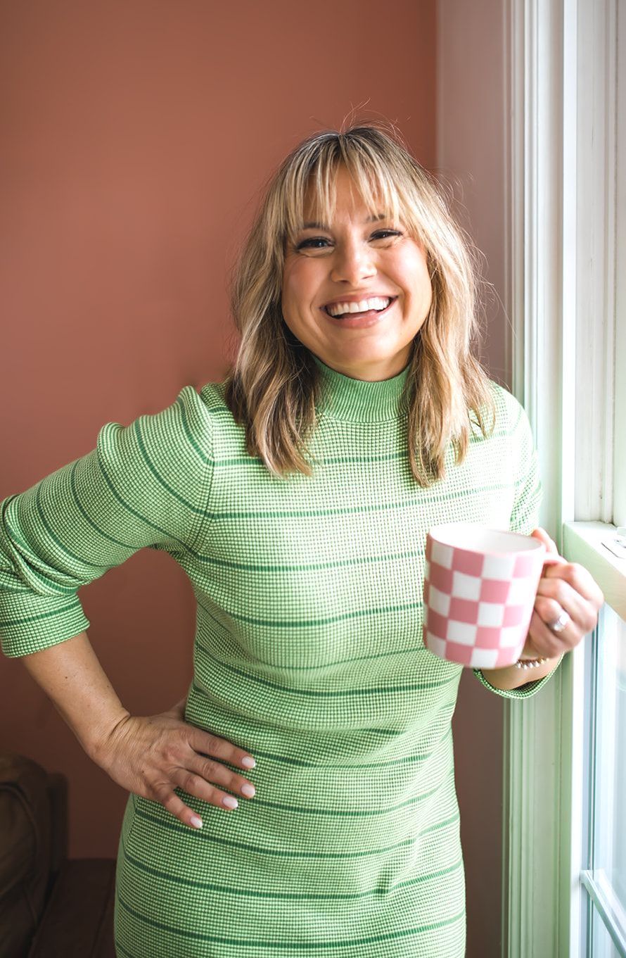 Amanda in a green dress is holding a cup of coffee and smiling.