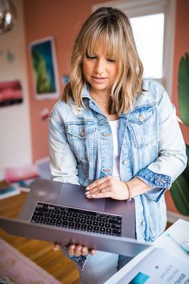 A woman in a denim jacket is holding a laptop computer.