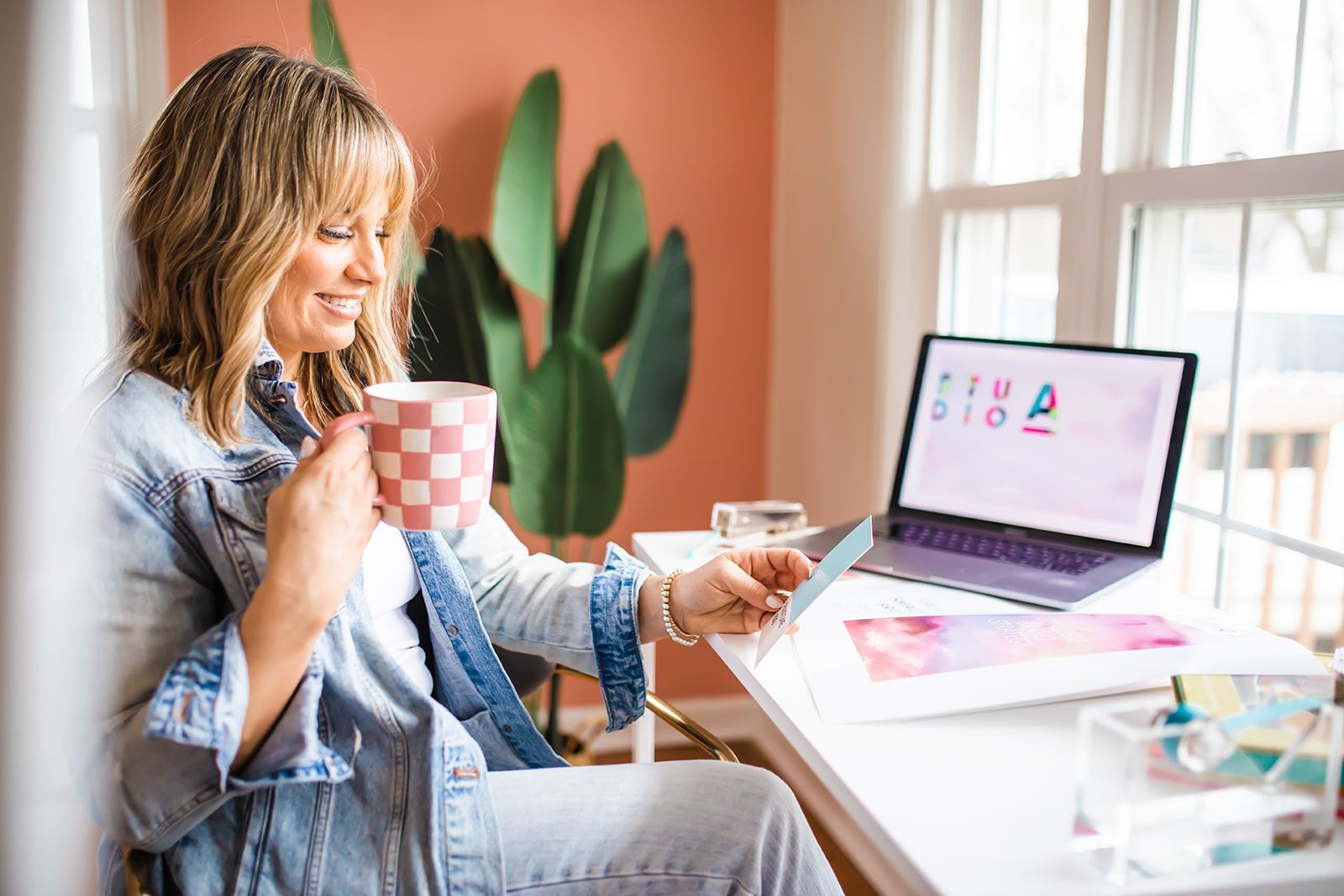 A woman is sitting at a desk with a laptop and a cup of coffee.