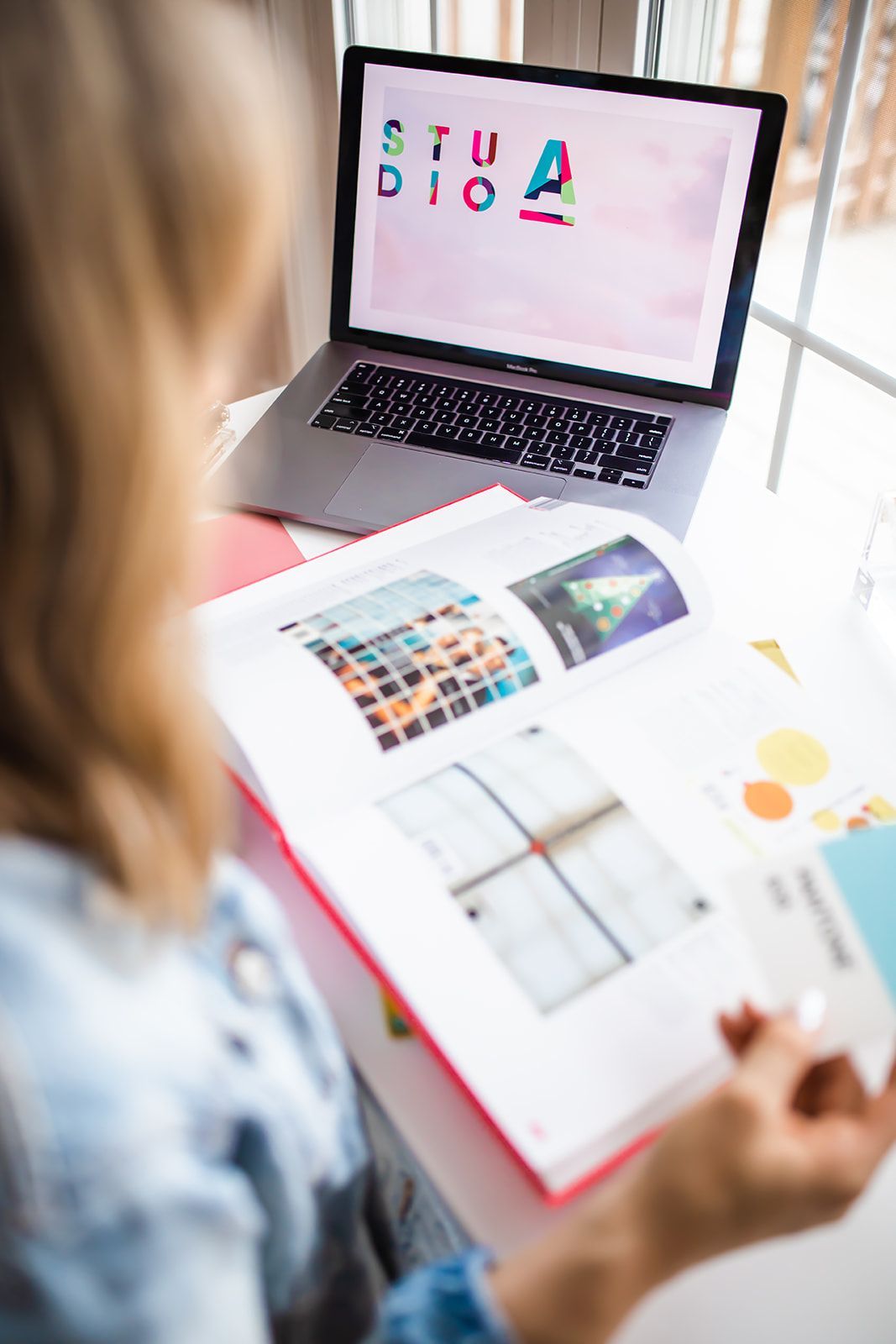 A woman is sitting at a table with a laptop and a book.