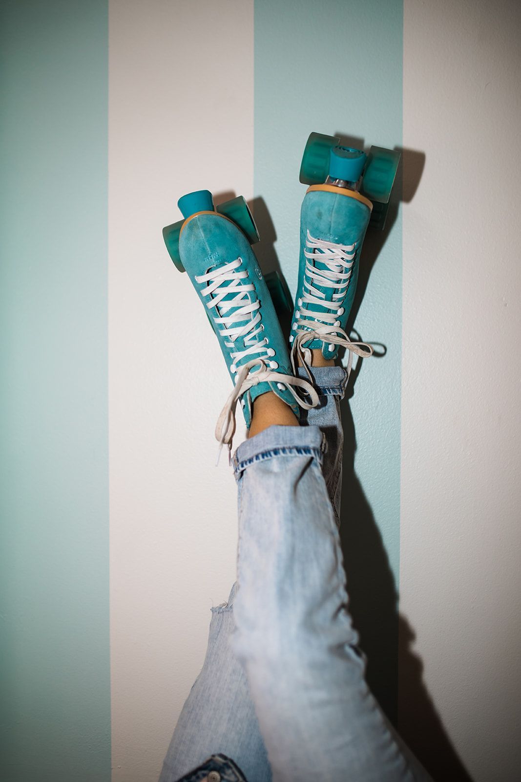 A person wearing blue roller skates with their legs crossed against a striped wall.