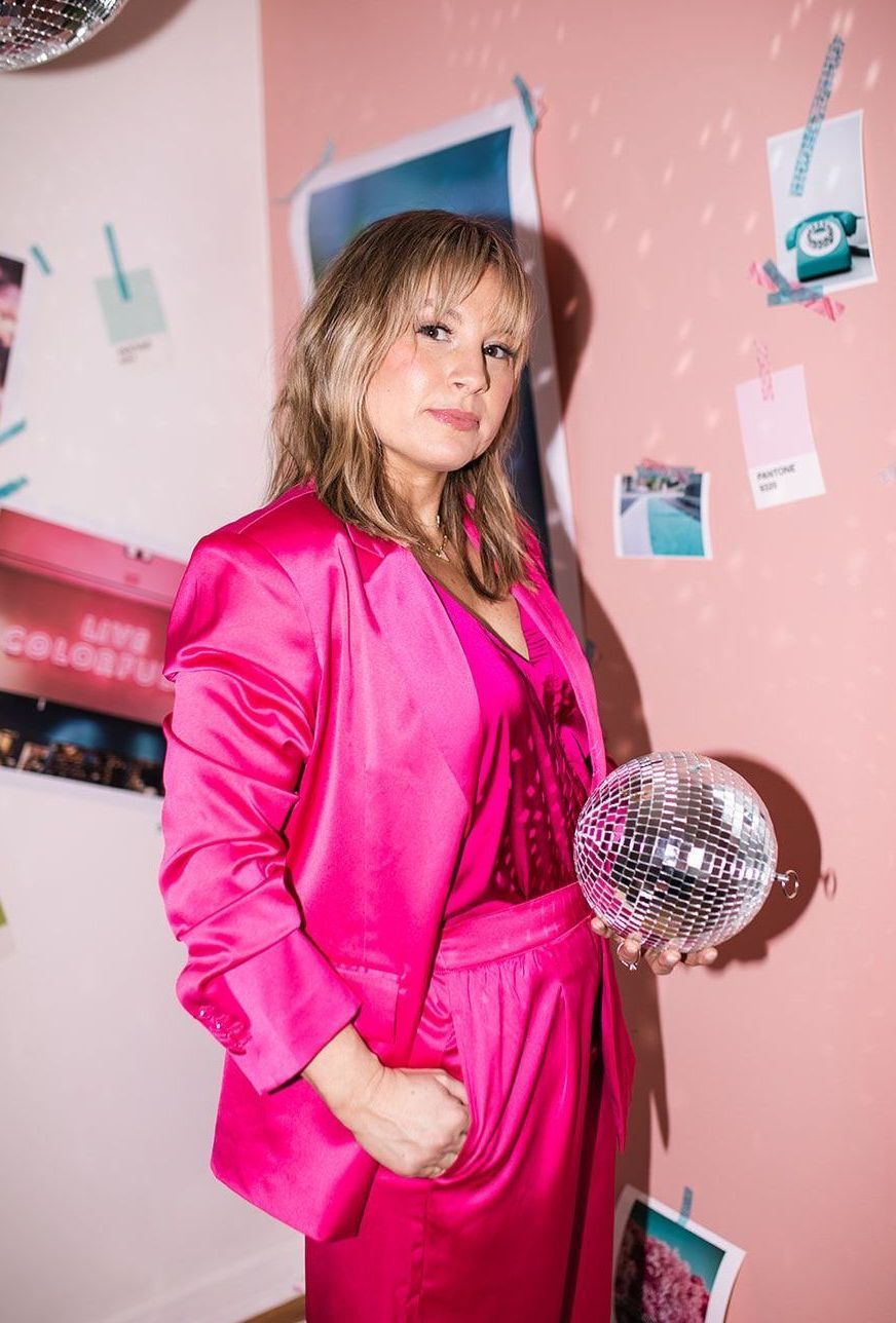 A woman in a pink suit is holding a disco ball.