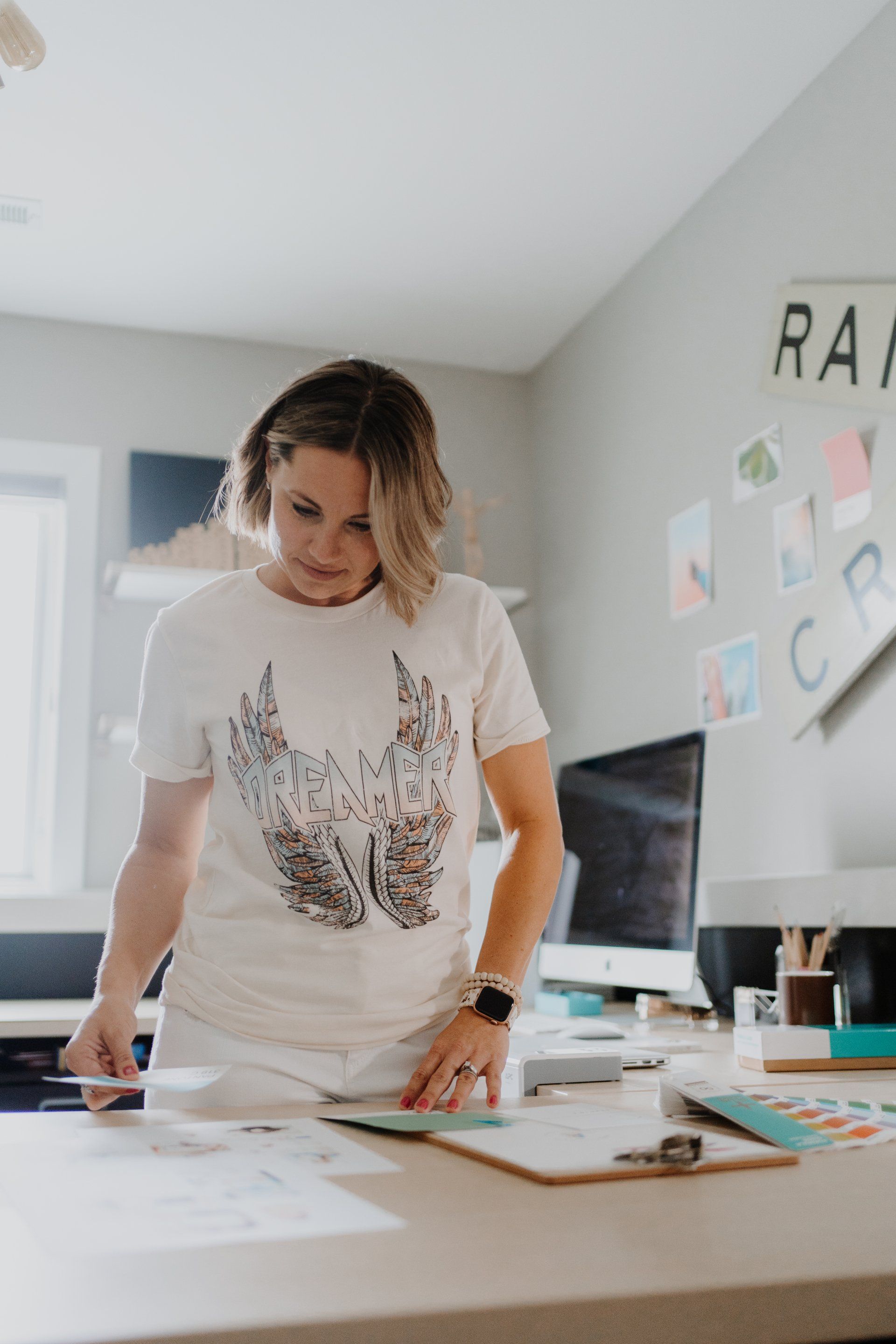 A woman in a white t-shirt is standing in front of a desk.