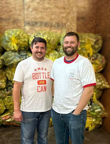 Two men are standing next to each other in front of a pile of bags.