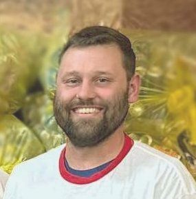 A man with a beard is smiling in front of a pile of bags.